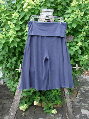 Barclay Thermal Fold Over Crop Pant Unpainted Deep Violet Size 1, featuring wide-leg, mid-calf length and a versatile fold-over waistband, displayed on a ladder amidst lush greenery.