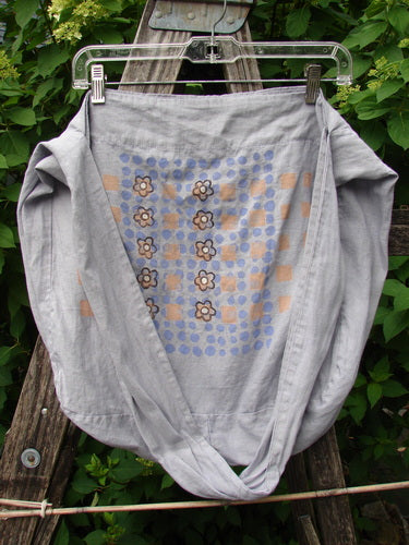 Barclay Linen Sling Tote Daisy Row Lavender OSFA draped on a wooden ladder, showcasing its lightweight linen fabric with stylized flower motifs over a grid of blue and peach dots.