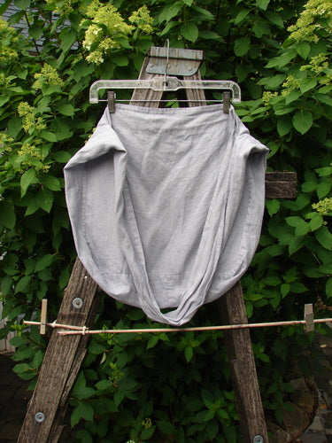 Barclay Linen Sling Tote Daisy Row Lavender OSFA, displayed on a weathered stepladder, showcases a wide shoulder sling and slouchy design. Made from lightweight linen with a daisy row theme.