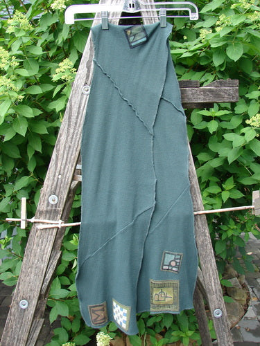 Barclay Thermal Patched Curvy Scarf Army Forest OSFA hangs gracefully, showcasing a patchwork design with curly edges and waffle texture, draped over a wooden ladder against lush greenery.