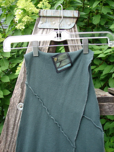 Barclay Thermal Patched Curvy Scarf in Army Forest OSFA, showcasing a green waffle-knit texture with diagonal seams and a camo-style patch, displayed on a hanger against a garden backdrop.