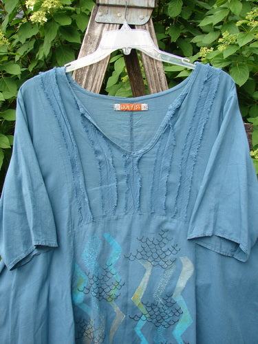 Barclay Batiste Flutter Bib Tie Back Dress features a teal-blue tunic with a scooped neckline and pintuck trim, displayed on a ladder, embodying Bluefishfinder.com's vintage-inspired, expressive style.