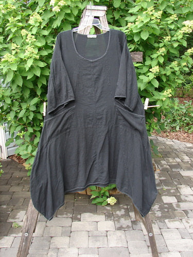 Barclay Gauze Urchin Bell Dress Unpainted Black Size 1 draped on a wooden ladder, showcasing its loose tunic style, scooped neckline, and large side pockets against a leafy hedge backdrop.