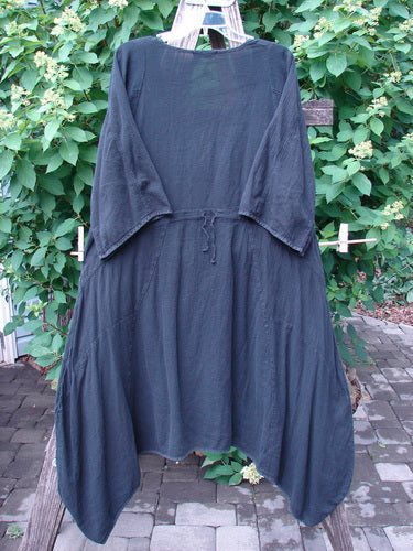 Barclay Gauze Urchin Bell Dress Unpainted Black Size 1, displayed on a wooden ladder, showcases wide three-quarter sleeves, an adjustable drawstring waist, and an uneven drapey hem against a natural outdoor setting.