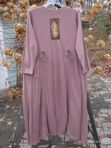 1998 Cornucopia Dress Fall Vegetable Eggplant Size 1. Long pink dress with vertical drawstrings, displayed on a wooden pole, showcasing intricate fall vegetable-themed paint and heavy bottom piece.