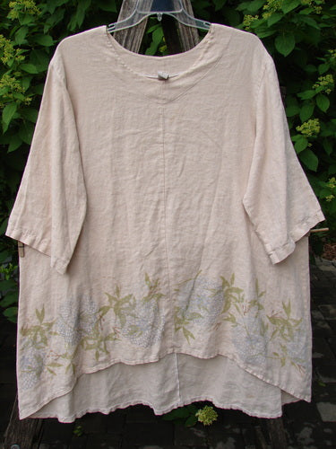 Barclay Linen Hi Low Tunic Top Bamboo Border Plantain Size 2, featuring a loose fit, rounded neckline, elbow-length sleeves, and a subtle leaf pattern. Displayed hanging outdoors against lush greenery.