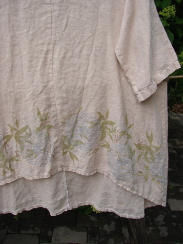 Barclay Linen Hi Low Tunic Top Bamboo Border Plantain Size 2 features a loose-cut design with elbow-length sleeves, adorned with pastel hydrangea-style blossoms along the hem, perfect for expressing individuality.