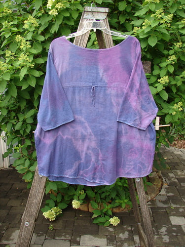 Barclay Gauze Round Bottom Tie Back Pocket Top in Mottled Purple Dusk, Size 2, hangs on a wooden stand, showcasing its loose fit and long sleeves, against a serene outdoor setting.