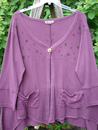 Barclay Patched Thermal Single Button Cardigan Tiny Square Murple Size 1, featuring a scoop/V-neck, wooden button, patch pockets with ruffle detail, and raw-edge seams, displayed outdoors against lush foliage.