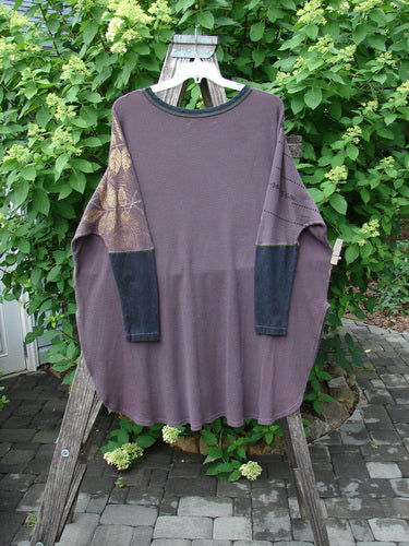 Barclay Thermal Contrast Revival Top Metallic Leaf Brum OSFA hangs on a wooden hanger, highlighting its loose fit, muted brownish-gray hue with darker cuffs, and gold-toned print on one shoulder.