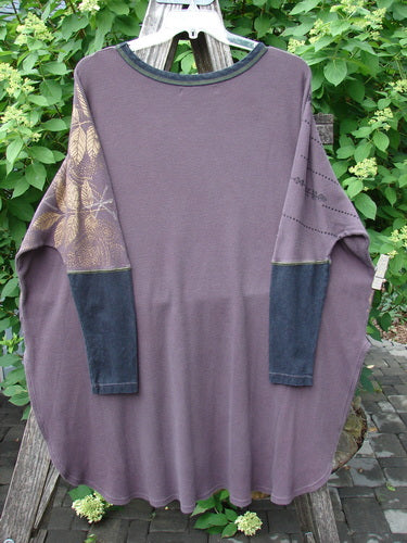 The Barclay Thermal Contrast Revival Top Metallic Leaf Brum OSFA is a loose-fit, muted purple tunic with decorative patterned sleeves, draped on a wooden ladder, embodying Bluefishfinder.com's vintage style.