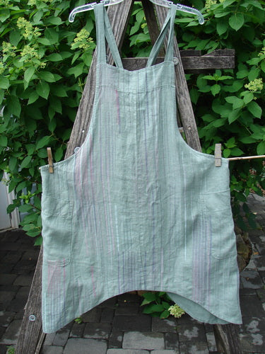 Barclay Linen Side Pocket Apron Jumper Verticals Sage Size 0 displayed on a wooden ladder outdoors, featuring adjustable cross-back straps, vertical stripes, a banded upper bib, and spacious side pockets.