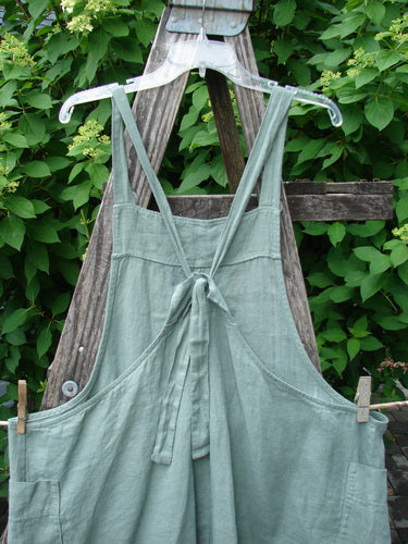 Barclay Linen Side Pocket Apron Jumper Verticals Sage Size 0 hanging on a ladder, showcasing crisscrossing straps, a waist tie, and roomy side pockets, reflecting Bluefishfinder.com's vintage, creative clothing ethos.
