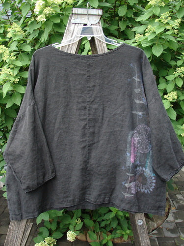 Barclay Linen Lantern Boxy Top Side Floral Black Size 1, featuring a loose-cut square shape, ¾-length sleeves, subtle floral print on one side, draped over a wooden stepladder against green foliage.