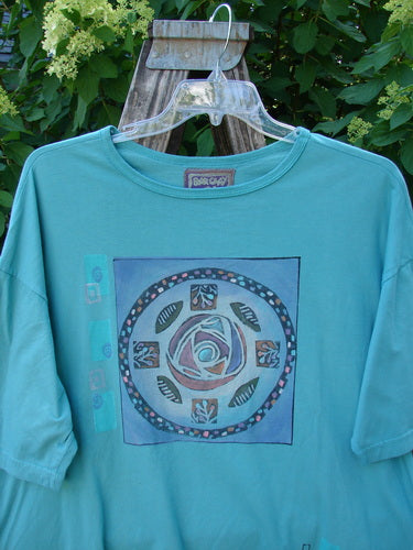 Barclay Short Sleeved Crop Box Tee Center Rose Aqua Size 3 displayed on a clear hanger outdoors, showcasing a stylized rose motif. The tee features an airy, oversized, boxy shape with generous short sleeves.