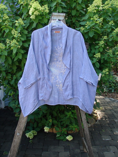 Barclay Linen Open Front Cheerful Cardigan Jacket Rear Starburst Iris Size 1, displayed on a wooden ladder outdoors, showcasing its dolman sleeves and varying hemline against a lush green backdrop.