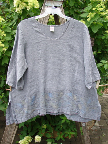 Barclay Linen Pinch Sleeve Curve Tie Back Top in Twig Grey, featuring a scoop neckline, elbow-length sleeves, and subtle border pattern, draped over a rustic ladder, embodying vintage Blue Fish individuality.