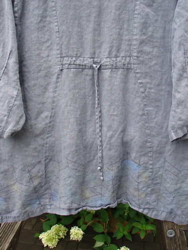 Barclay Linen Pinch Sleeve Curve Tie Back Top in Twig Grey Size 1, featuring a long-sleeved tunic style with adjustable back tie and geometric embroidery along the hem, hanging above hydrangea blossoms.