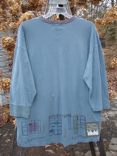2000 V Neck Grid Top Direction Travel Puddle Size 1, displayed on a mannequin, featuring a V neckline, single cuff, A-line shape, vented sides, and rounded bottom sweep. Made from organic cotton.