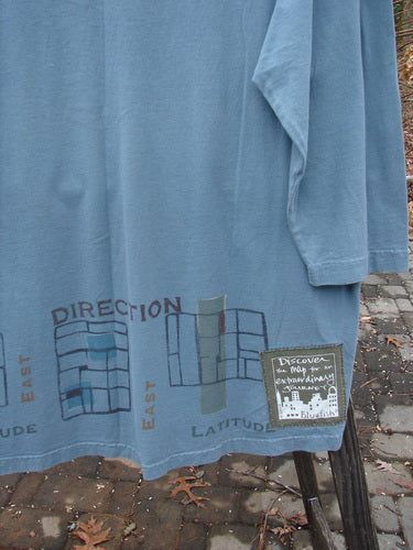 2000 V Neck Grid Top Direction Travel Puddle Size 1 hanging on a clothesline, showcasing a unique white and black patch design, organic cotton fabric, and distinctive V neckline with single cuff.