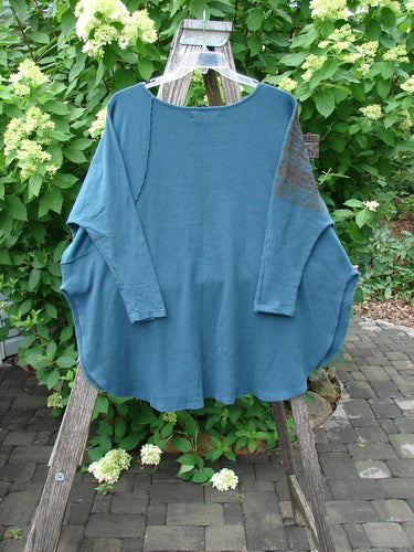 Barclay Thermal Monte Verde Vented Tunic Grid Blend Tealen OSFA displayed on a wooden ladder outdoors, showcasing its oversized fit, rounded neckline, side vents, and contrasting stitchery details against a natural backdrop.