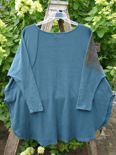 Barclay Thermal Monte Verde Vented Tunic Grid Blend Tealen OSFA, displayed on a wooden ladder, features a relaxed bat-wing silhouette, uneven hem, and ribbed sleeve accents in a garden setting.