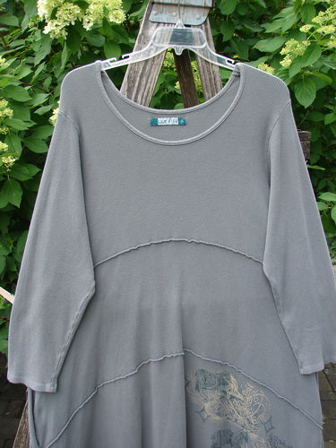 Barclay Thermal Exterior Stitch Three Tier Dress Forest Friend Grey Day Size 2, shown hanging on a clear hanger, features horizontal seaming, subtle hem embroidery, and is displayed against leafy shrubs.