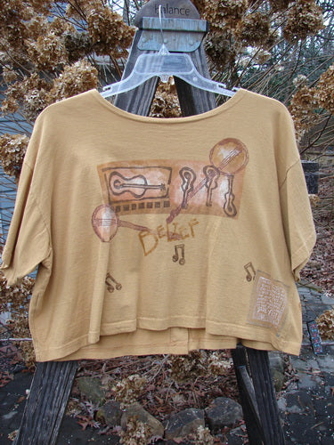 1994 Song Top Make Music Dijon Size 2: Tan shirt with wide crop box shape, shallow neckline, oversized front painted pocket, and music-themed drawing, featuring matching oversized buttons and Blue Fish Poetry Patch.