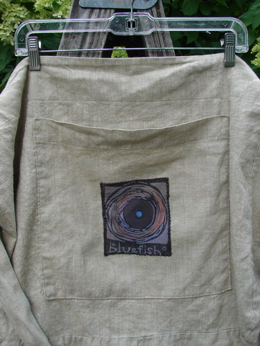 Barclay Patched Linen Pocket Tote Sling Window Door Wheat OSFA features a wide shoulder sling, slouchy design, and large front pocket with a concentric circle graphic and Bluefish text.