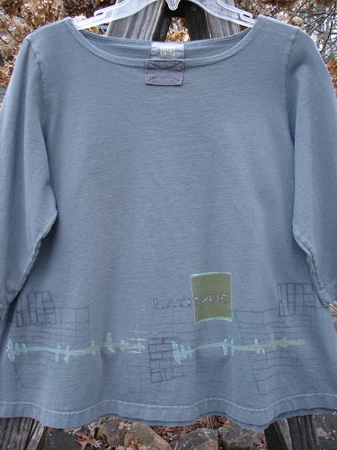 2000 Parklands Tee Top Latitude Iron Size 1: Slate-gray long-sleeve shirt with a scooped neckline, embroidered LATITUDE patch, stylized graphics along the hem, and stitched patches. Organic cotton, 3/4 sleeves, flared shape.