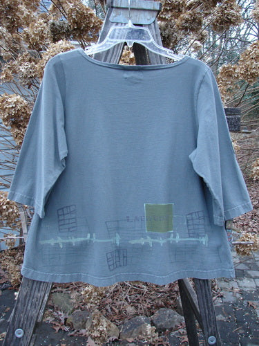 The 2000 Parklands Tee Top Latitude Iron Size 1 features a loose fit with three-quarter sleeves, a slightly flared shape, and subtle graphic prints along the hem, hanging on a wooden ladder.