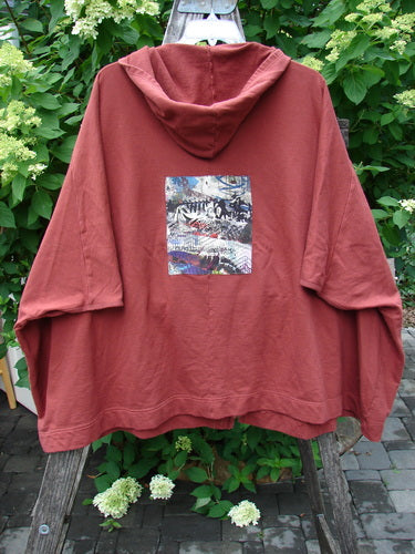 Barclay PMU Patched Hooded Postcard Zipper Jacket Vest in Deep Brick, oversized with a cozy hood, dolman shoulders, abstract rear graphic, and varying hemline, displayed outdoors on a wooden ladder.