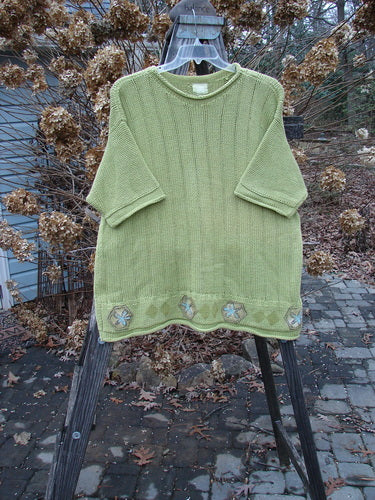 1999 Spring Pullover Tunic Sweater Kiwi Size 2 displayed on a wooden swing, showcasing its A-line shape, varied vertical textures, and fully painted hem with drop shoulders and a rolled neckline.