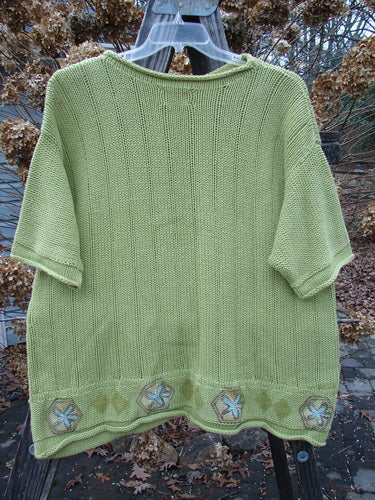 1999 Spring Pullover Tunic Sweater Kiwi Size 2 displayed on a clothes rack, featuring a lively A-line shape, varied vertical textures, rolled neck, sleeves, and hemline, with a distinctive painted hem circumference.