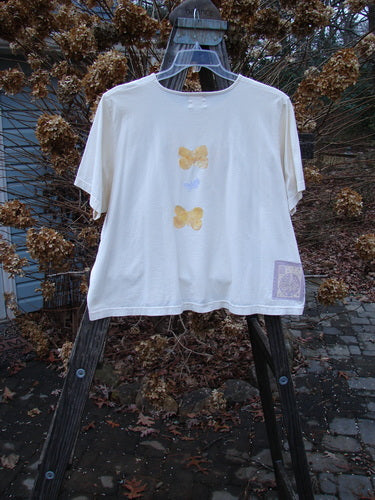 1999 Light Weight Short Sleeved Crop Tee Butterfly Natural Size 2 displayed on a swinger, showcasing butterfly designs, short sleeves, and a rounded neckline.