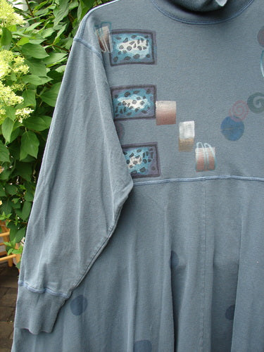 The 1996 Enchantment Dress Polka Path Mirror Size 2 features a slate-gray/blue tunic style with abstract patterns, ribbed turtleneck, empire waist, and expansive sweep, hanging amidst greenery.