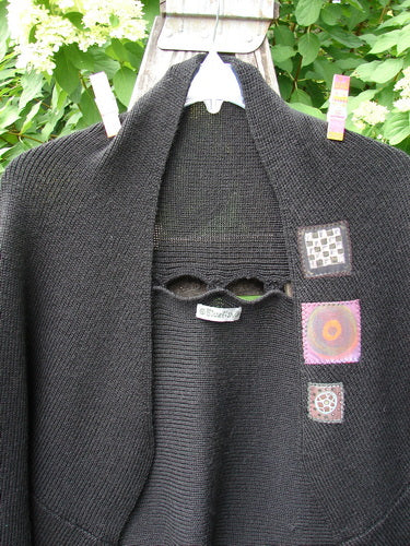 Barclay Patched Alpaca Rear Window Shrug Black OSFA, hand-knit with unique eye openings and decorative patches, hangs outdoors, showcasing its creative, vintage-inspired design synonymous with BlueFishFinder's expressive clothing line.