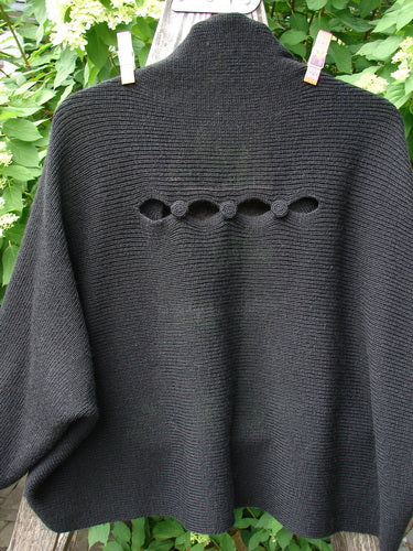 Barclay Patched Alpaca Rear Window Shrug Black OSFA draped on a rail, showcasing hand-knit texture, garter stitch body, rolled neckline, oval eyelet details, and unique buttoned collar.