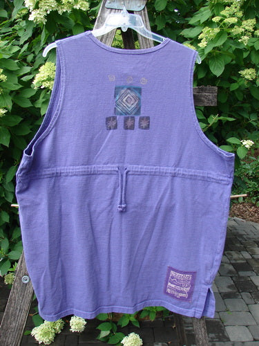 1996 Symbol Vest Star Rain Byzantium Size 2 hangs on a clear hanger, featuring a waist drawcord, geometric panel on the upper back, and a woven label near the hem, displayed on a wooden bench.