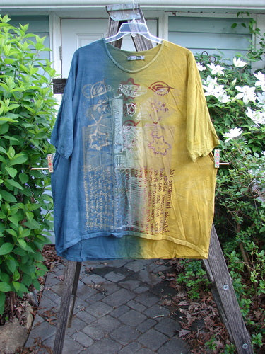 Barclay Tournesol Tunic Harmonic Hillside Mottled Dawn OSFA features a mid-length design, drop shoulders, loose three-quarter sleeves, rounded neckline, varying hemline, and artistic script theme on an earthen backdrop.