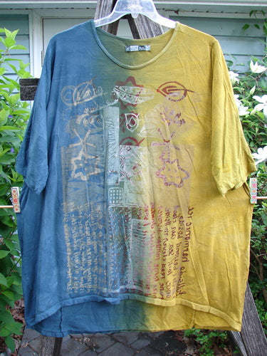 Barclay Tournesol Tunic Harmonic Hillside Mottled Dawn OSFA: A versatile tunic or mid-length dress with drop shoulders, loose three-quarter sleeves, rounded neckline, and varying hemline, showcasing artistic script on an earthen backdrop.