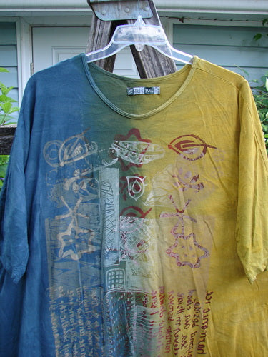 Barclay Tournesol Tunic Harmonic Hillside Mottled Dawn OSFA features a loose, mid-length design with drop shoulders and three-quarter sleeves, showcasing an artistic script theme on an earthen backdrop.