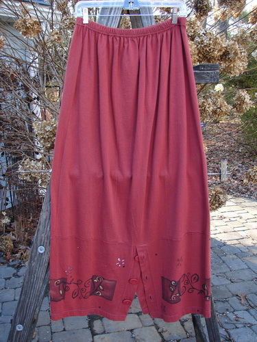 1997 Hearth Peplum Button Duo Vines Brick Size 2: A red skirt with an elastic waistline, oversized buttons, side pockets, and garden vine-themed paint displayed on a pole.