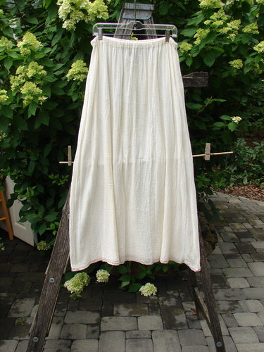 1998 Gauze Under Skirt Unpainted Cloud Size 2, cream tiered skirt in gauzy fabric, hangs outdoors, showcasing its full A-line shape and flowing design, highlighted by pink silk ribbon hem.