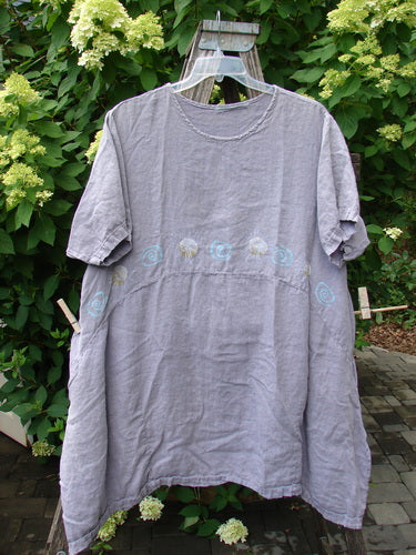 1997 Urchin Dress Sun Ray Swirl Sea Urchin Size 2, featuring a loose fit, short sleeves, and pale blue embroidery on the waistline, displayed outdoors among green shrubs and hydrangeas.