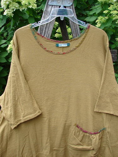 Barclay Gauze Round Bottom Tie Back Pocket Top Ditsy Daisy Golden Size 2, featuring elbow-length sleeves, scoop neckline, and a small gathered front pocket, displayed on a hanger against a rustic backdrop.