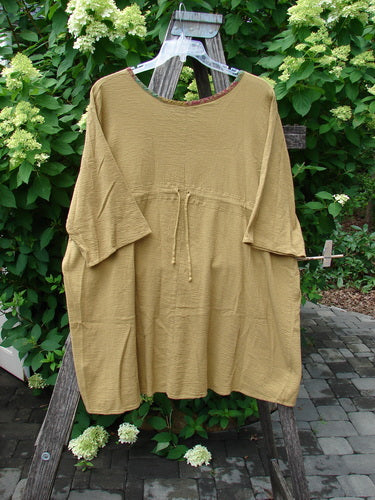 Barclay Gauze Round Bottom Tie Back Pocket Top Ditsy Daisy Golden Size 2 displayed on a wooden hanger, draped over a ladder in a garden setting. The tunic features elbow-length sleeves and a waist drawstring.