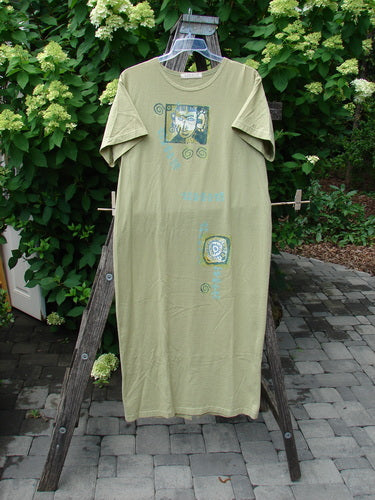 1997 Aquavella Dress Modern Gal Pear Size 1: Olive-green T-shirt-style dress with short sleeves, graphic prints, and a scooped neckline. Displayed on a hanger outdoors, highlighting its vintage charm and organic cotton fabric.