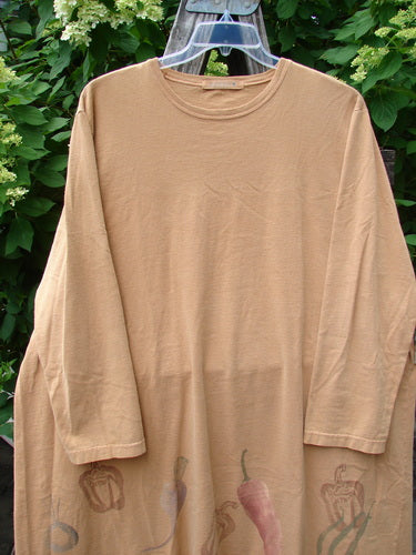 1998 Vegetable Tunic Top Bountiful Garden Ochre Size 2, featuring an A-line shape and rolled neckline, showcases a vibrant chili and bell pepper hemline design, hanging against lush green foliage on a clear hanger.