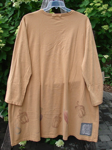 1998 Vegetable Tunic Top Bountiful Garden Ochre Size 2, featuring a softly scooped neckline and bell pepper motifs along the hem, displayed on a hanger against a green foliage backdrop.